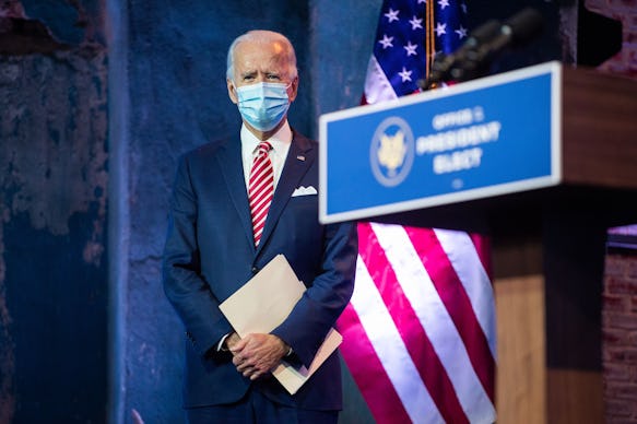 Joe Biden with a mask over his mouth, holding a white folder