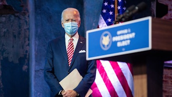 Joe Biden with a mask over his mouth, holding a white folder