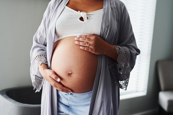 Pregnant woman with hands on belly, in a story about the signs baby is coming before due date.