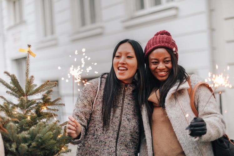 Two young women hold sparklers next to their new Christmas tree while adventuring around the city.