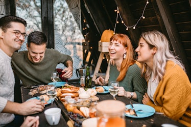 A group of friends enjoys a Thanksgiving meal around a picnic table outdoors.