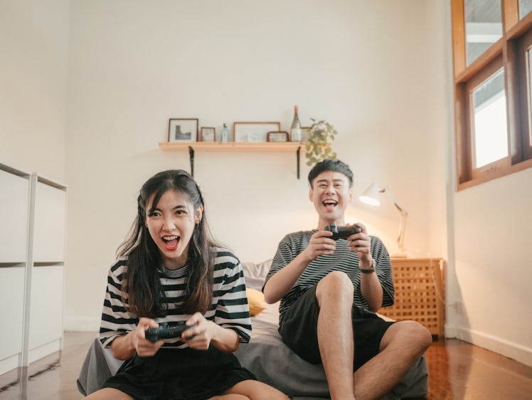 A young Asian couple laughs and gets competitive while playing video games at home.