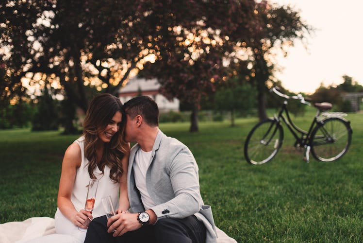 A happy couple enjoys a glass of wine on a bicycle picnic out in the park at sunset.