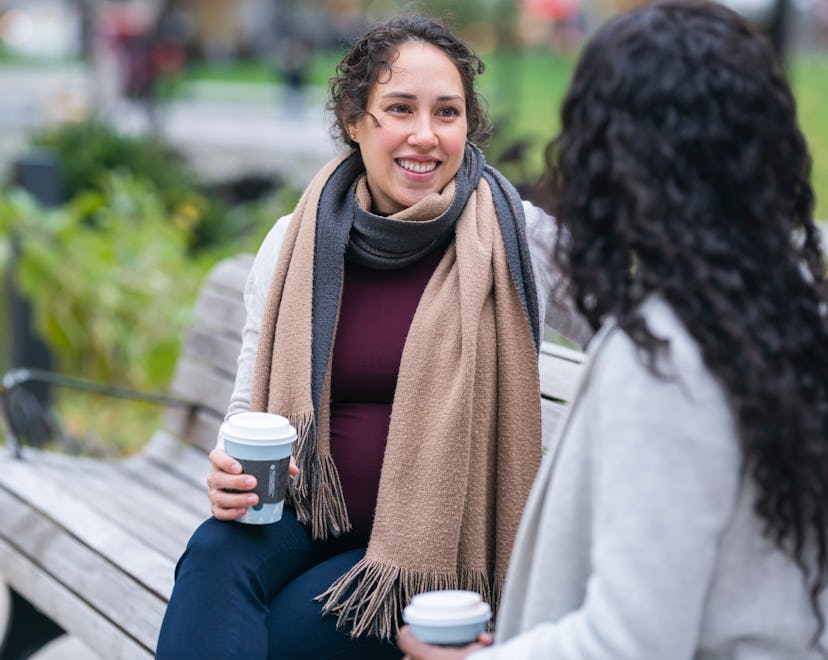 pregnant woman and friend drinking coffee on bench