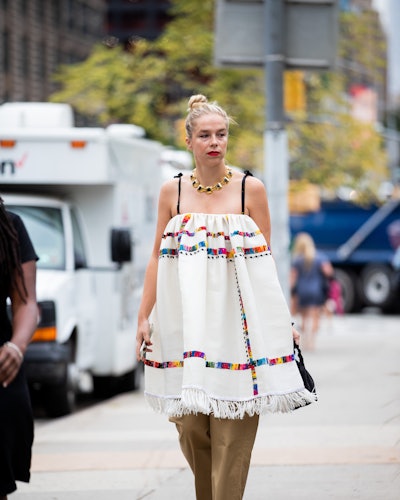 Chloe walking the street in a white embroidered dress and olive green wide-leg pants.