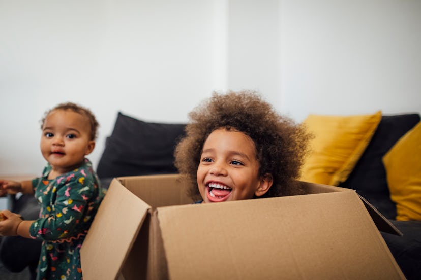 A toddler and a kid in a carton box playing in a living room