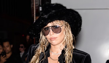 Miley Cyrus wears a black furry hat and sunglasses on the red carpet with a wet hair style. 