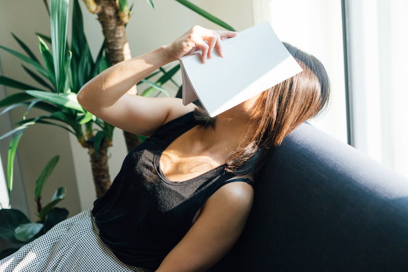 A woman naps on a couch with a book over her face during Thanksgiving week. Exercise guilt is real; ...