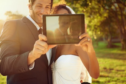 A happy couple snaps a selfie with their tablet outside at sunset. 