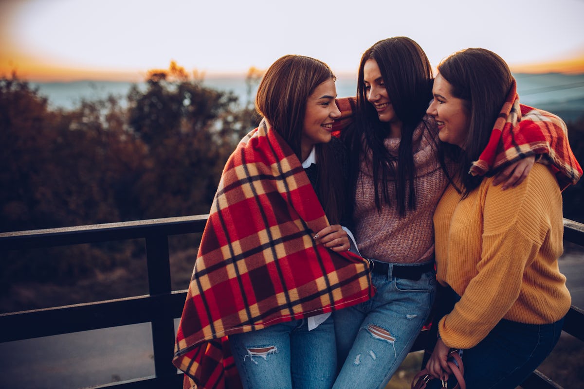 Three happy friends huddle close together on a balcony in the fall at sunset.