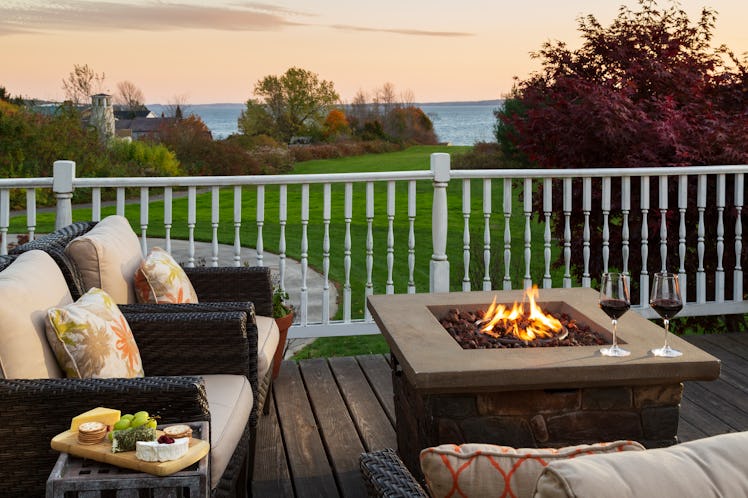An outdoor fire pit has two couches next to it, in addition to a little table with a cheese board.