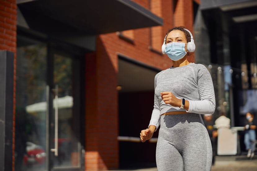 A person wears a mask, headphones, and a grey running outfit while jogging in the city. Spice up you...