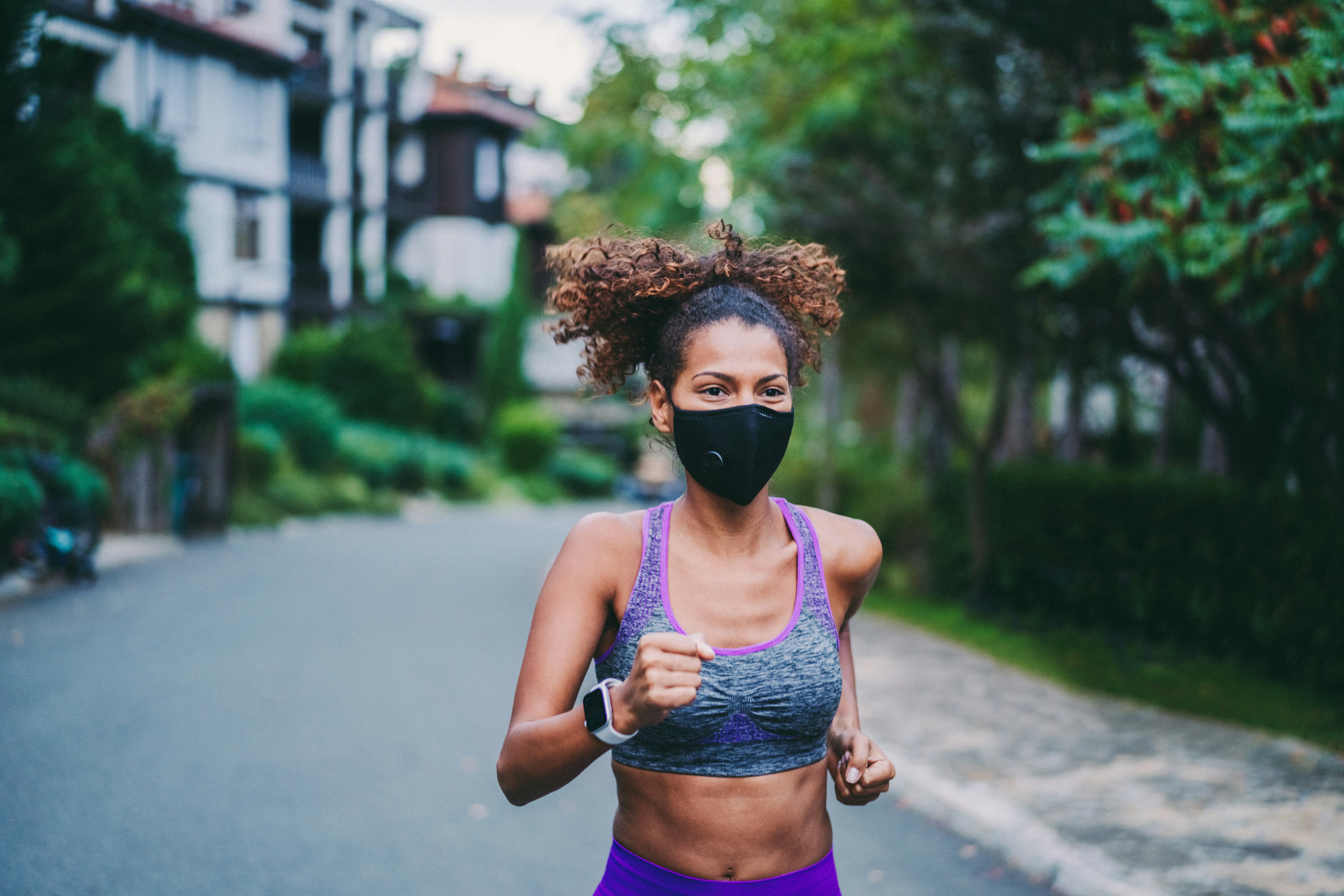 A person with natural hair and a sports bra wears a black mask while running outside. Your run doesn...