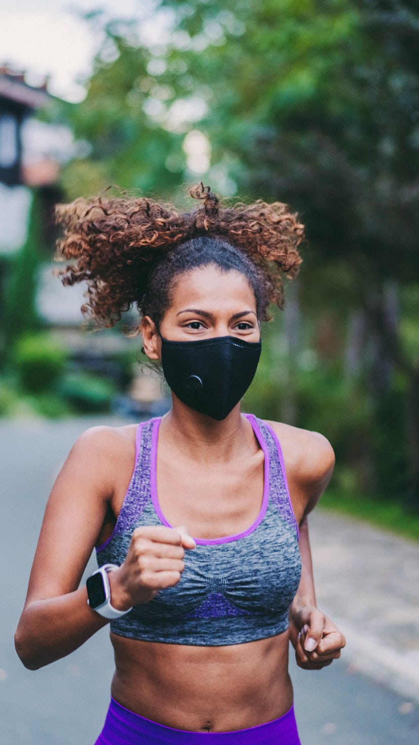 A person with natural hair and a sports bra wears a black mask while running outside. Your run doesn...
