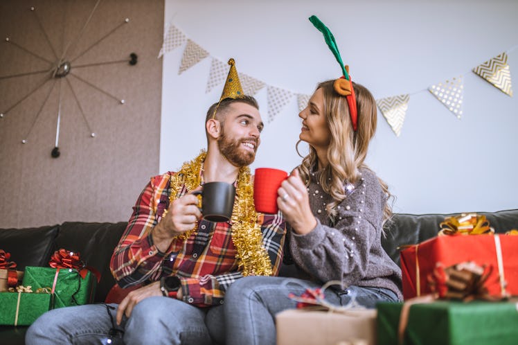 A happy couple toasts their Christmas mugs while surrounded by presents on Christmas morning.