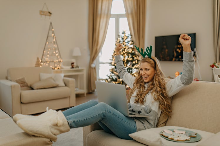 A happy woman who's dressed up for Christmas looks at her laptop on the couch.