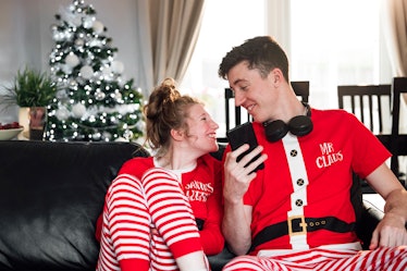 A happy couple relaxes at home on the couch in matching holiday PJs.