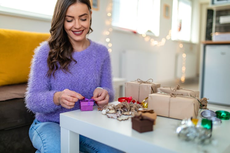 A girl is having fun making her Christmas gifts by decorating presents with bows, ribbons, brown pap...