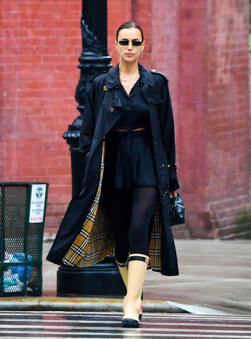 Irina Shayk styling beige rubber rain boots with a black dress and a trench coat