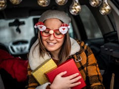 A woman wearing Santa glasses, holds onto two wrapped Christmas presents. 