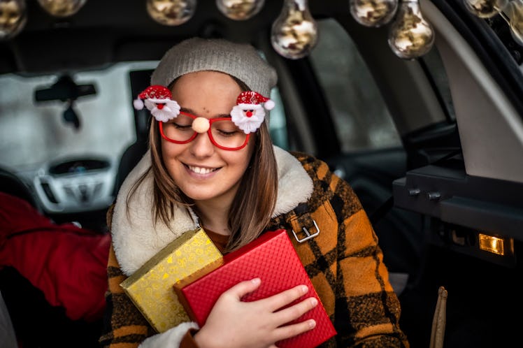 A woman wearing Santa glasses, holds onto two wrapped Christmas presents. 