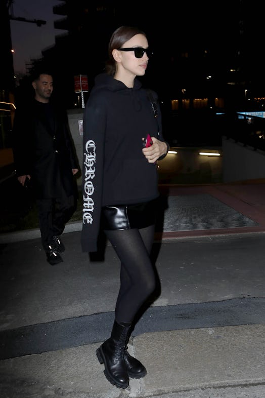 Irina Shayk posing in a black hooded sweatshirt and mini skirt paired with combat boots