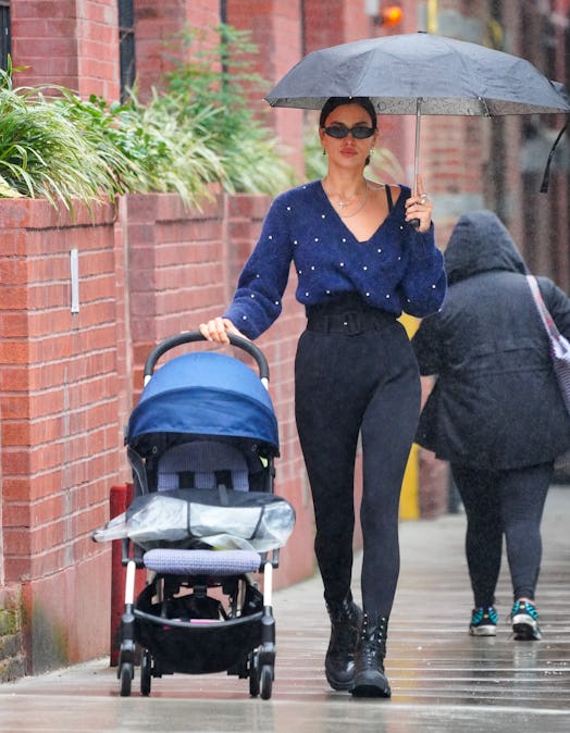 Irina Shayk pushing baby strollers while wearing a blue sweater and high-waisted fitted pants paired...