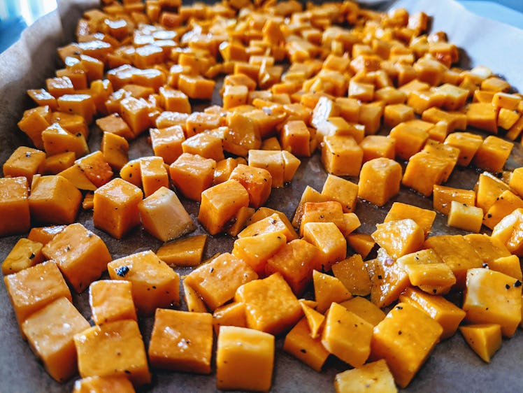 Cubes of butternut squash lay on a large baking pan while covered in olive oil and spices.