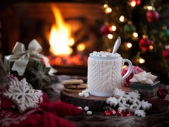 A holiday mug is surrounded by Christmas decor and fake snowflakes, with a fireplace and Christmas t...