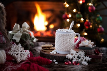 A holiday mug is surrounded by Christmas decor and fake snowflakes, with a fireplace and Christmas t...