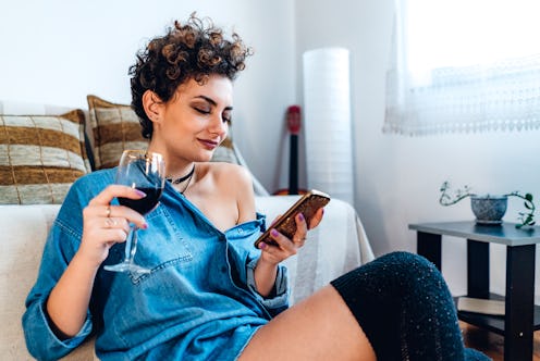 A woman sits on her couch with a glass of wine. Here's how one glass of wine affects your body.