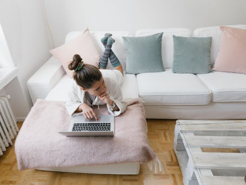 A woman does work on her laptop while lying on the couch. Work-from-home setups can mess up work-lif...