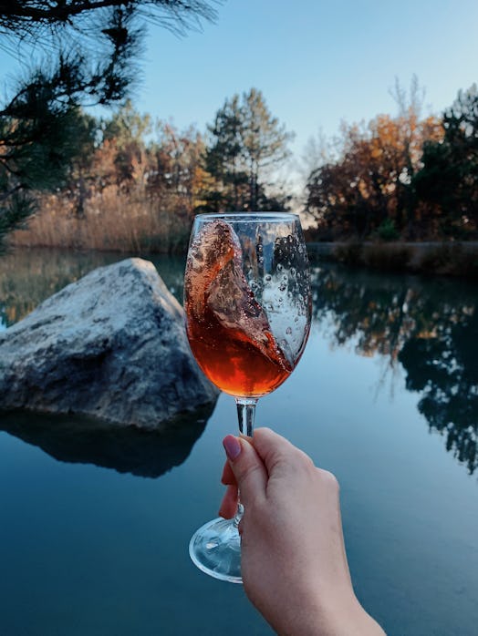 A woman holds up a glass of wine in front of a lake with fall foliage. Doctors explain what happens ...