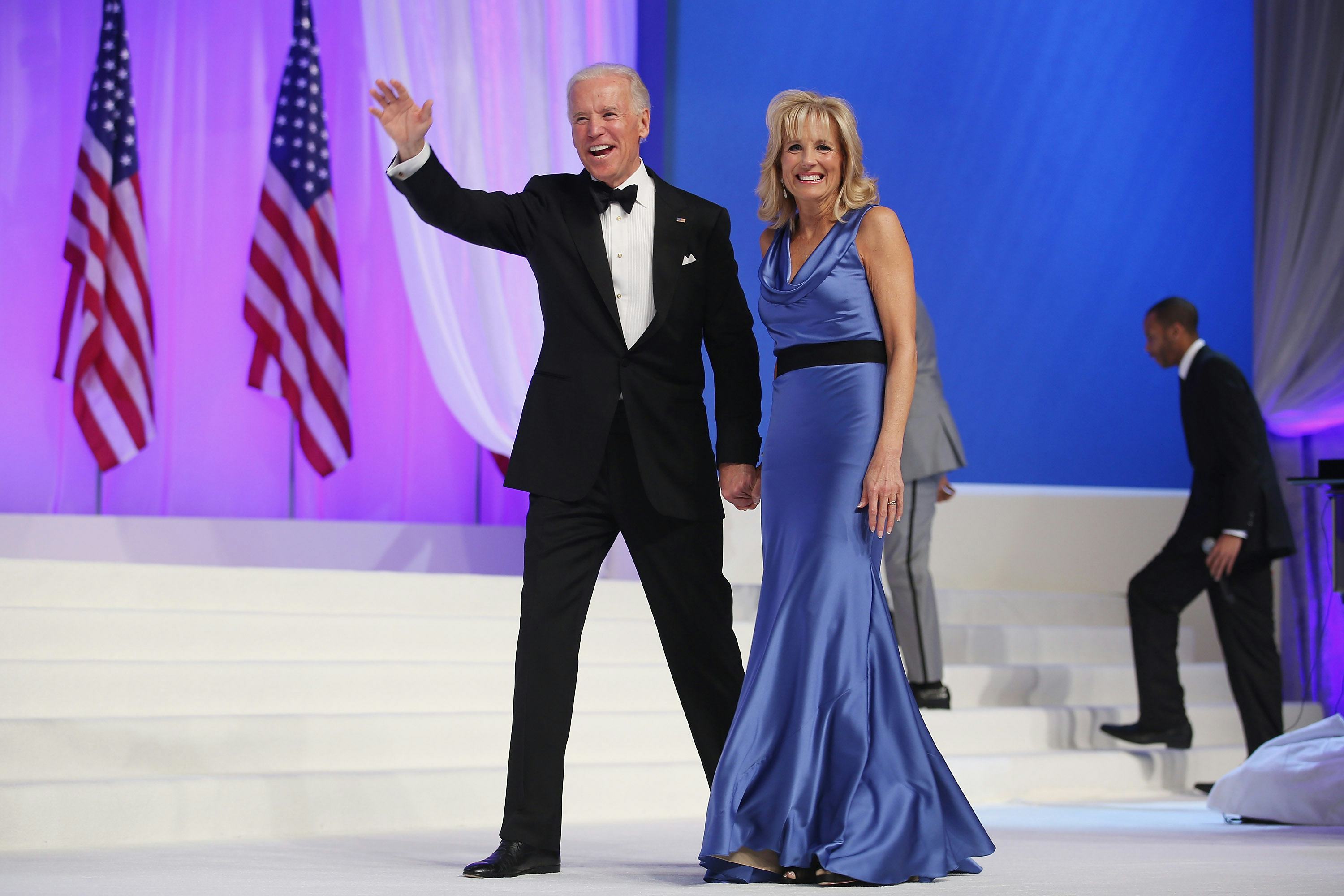 Joe Biden in a formal suit walking with Jill Biden in a light blue silk gown