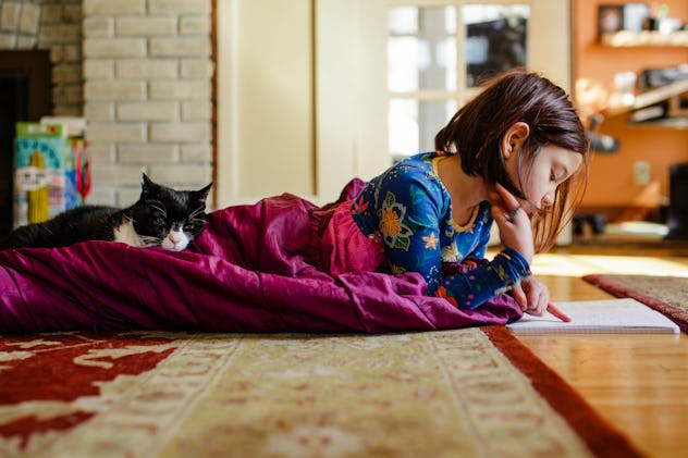 A little girl lying stomach down on the floor wrapped in a blanket and doing her homework with a car...