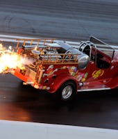 Red truck spitting flames out of its exhaust on a race track.