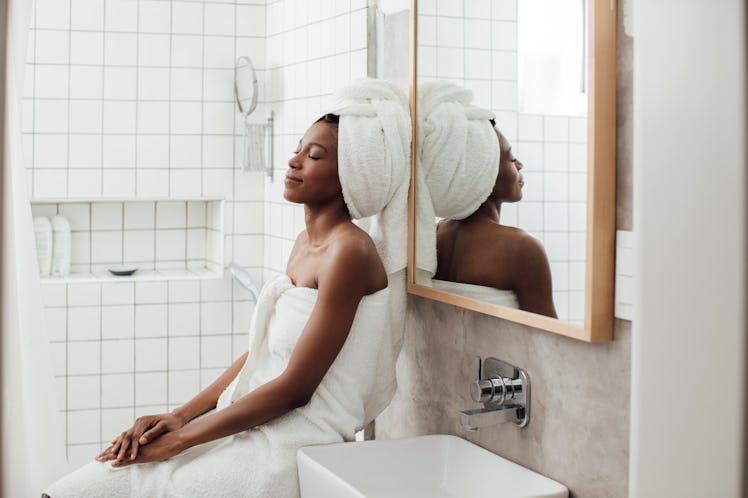 A happy woman relaxes in a bath towel in her bright bathroom.
