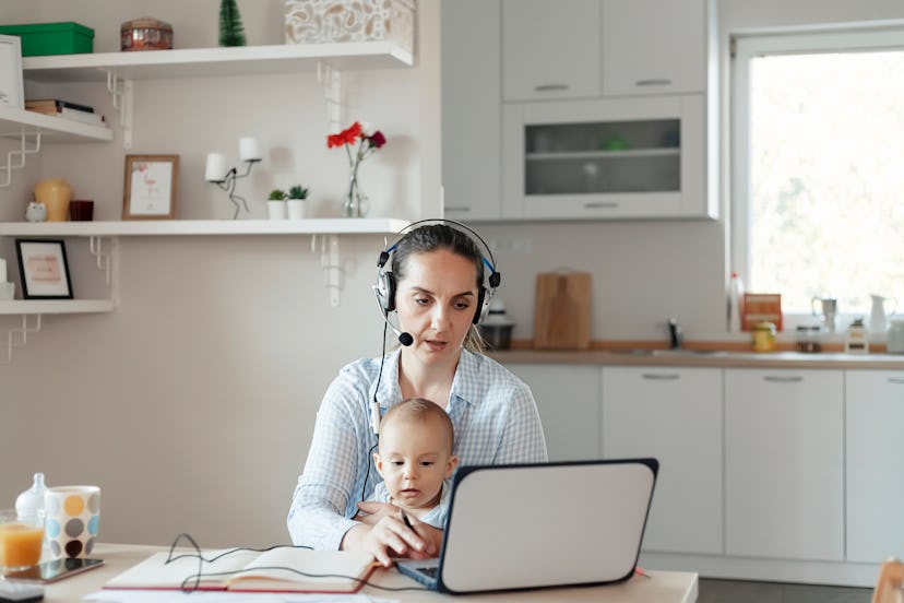 Mother working on her laptop with a headset on and a baby in her lap.