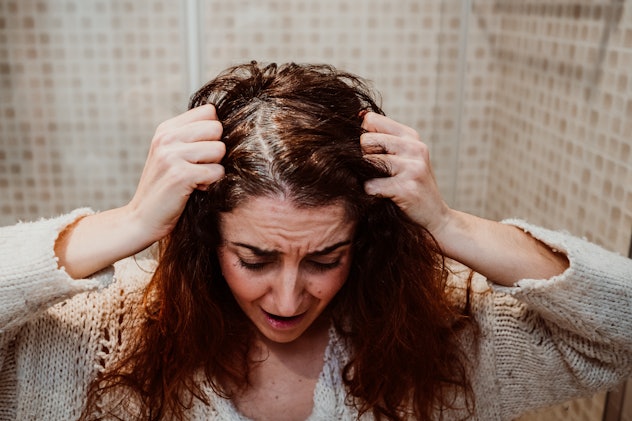 Woman in a bathroom looking down sadly with clenched fists on either side of her head.