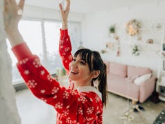A young woman hangs holiday lights in her apartment that's very cozy and minimalistic.