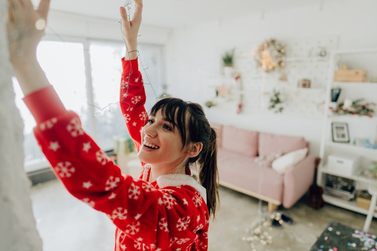 A young woman hangs holiday lights in her apartment that's very cozy and minimalistic.