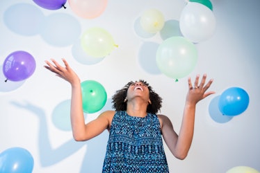 A happy woman admires balloons falling around her. 
