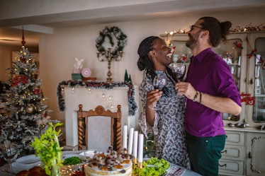 A happy couple embraces and holds their glasses of wine in a cozy Christmas home.