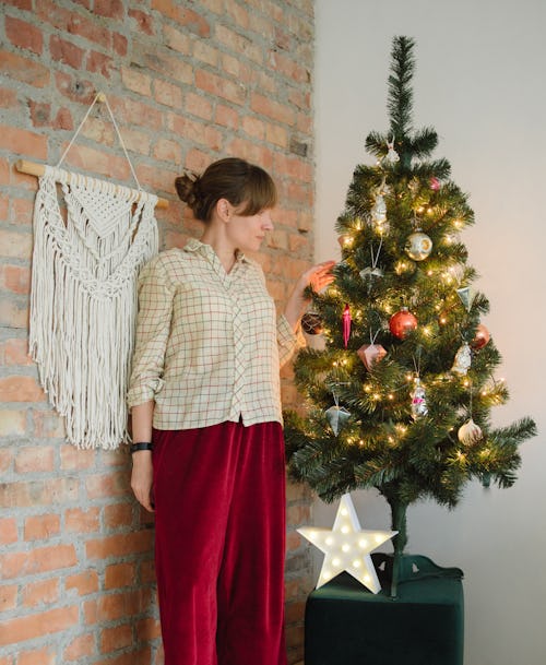 A woman in a sweater and red pants stands next to a small christmas tree. Experts share advice for f...