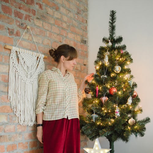 A woman in a sweater and red pants stands next to a small christmas tree. Experts share advice for f...