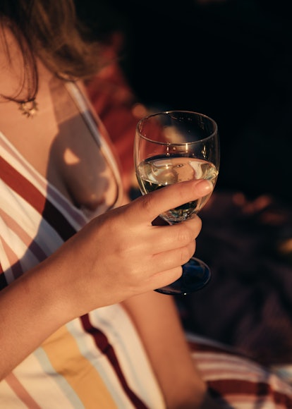 A young woman holds a champagne glass in her hands at golden hour.