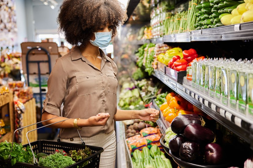 A woman buys groceries while wearing a mask. Doctors explain the best time to go grocery shopping du...