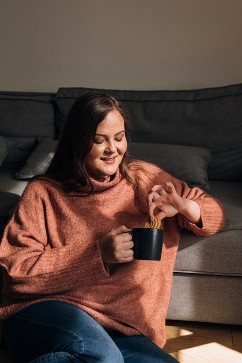 A woman in a cozy pink sweater drinks a mug of hot chocolate. Dietitians explain hot chocolate's hea...