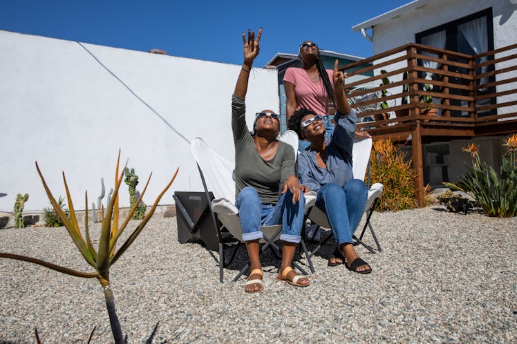 Three women look up at the solar eclipse in their solar eclipse glasses.