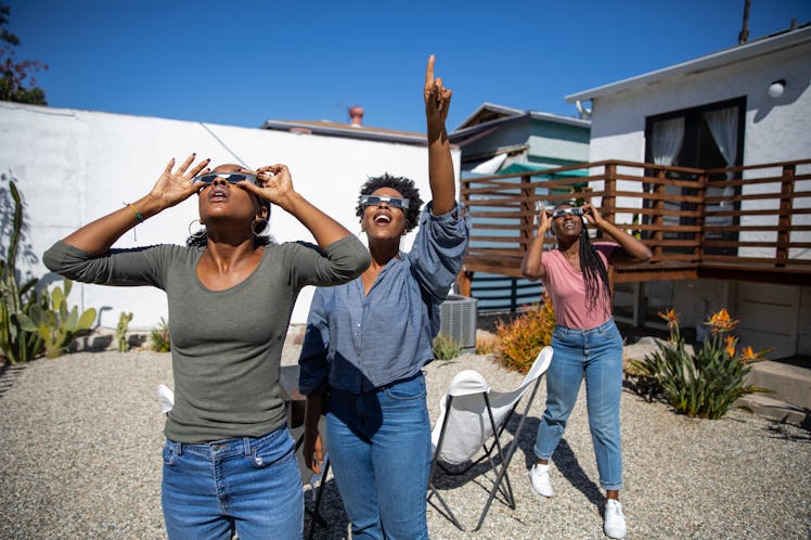 Three happy women gaze up at the solar eclipse in their solar eclipse glasses.